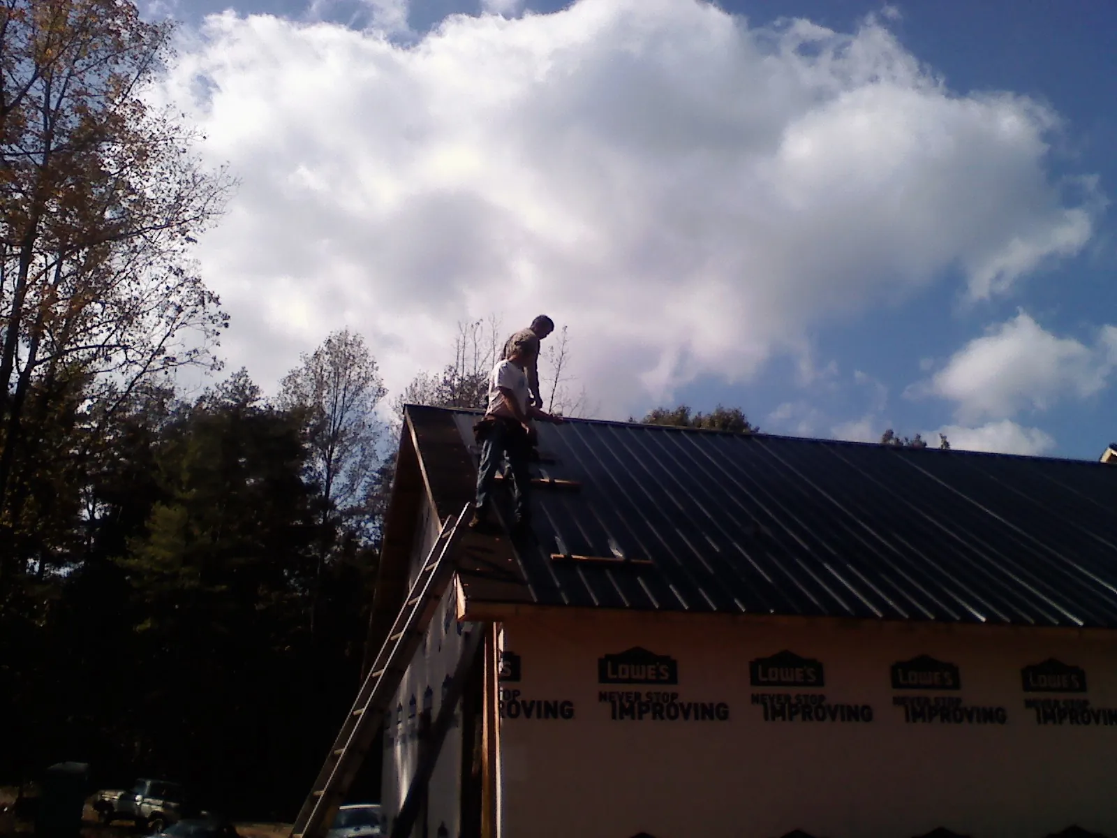 Roofer fastening dark metal panels high against a cloudy sky, from a Roof Inspection job in Hampton